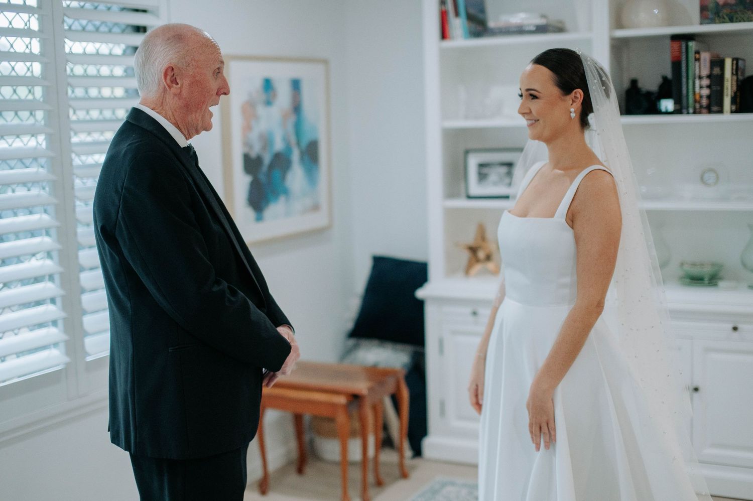 An emotional moment between the bride in a white dress and a person in a black suit during wedding preparations.