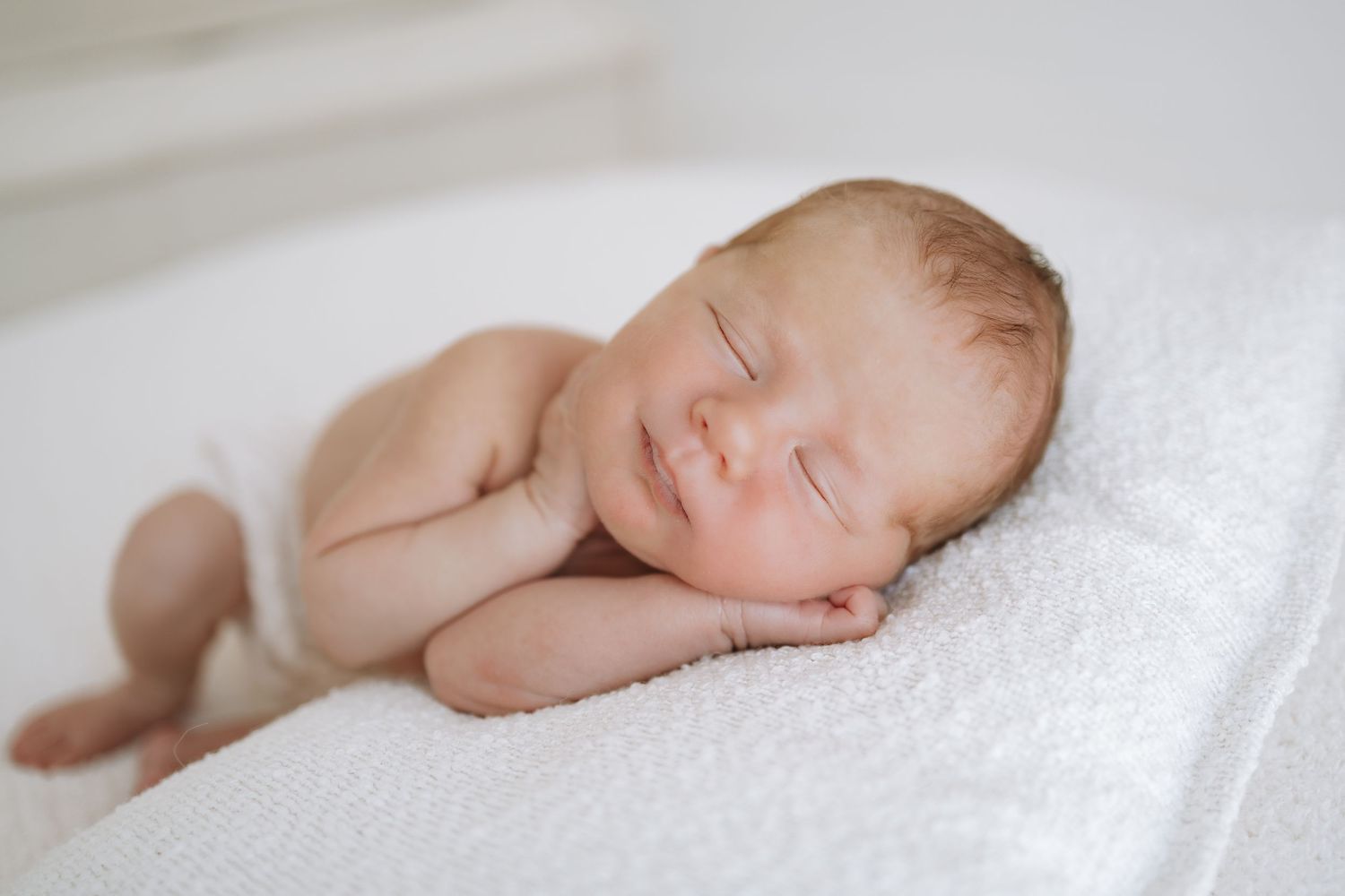 Series of artistic newborn portraits showing sleeping baby on white textured backdrop in natural light.