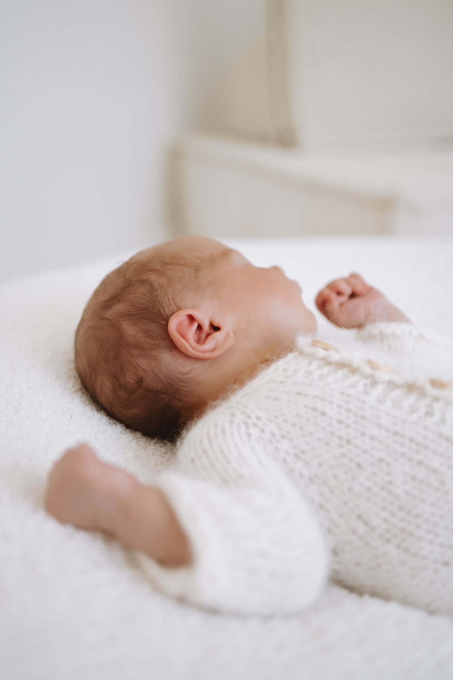 Peaceful newborn baby sleeping in soft white knit blanket against neutral background.