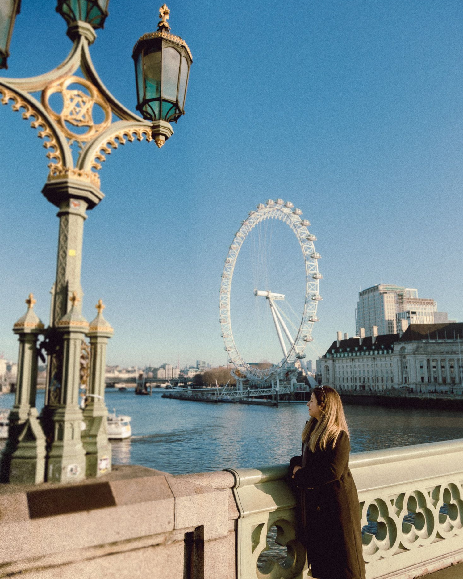 View of the London Eye from ornate bridge with decorative lamppost in foreground.