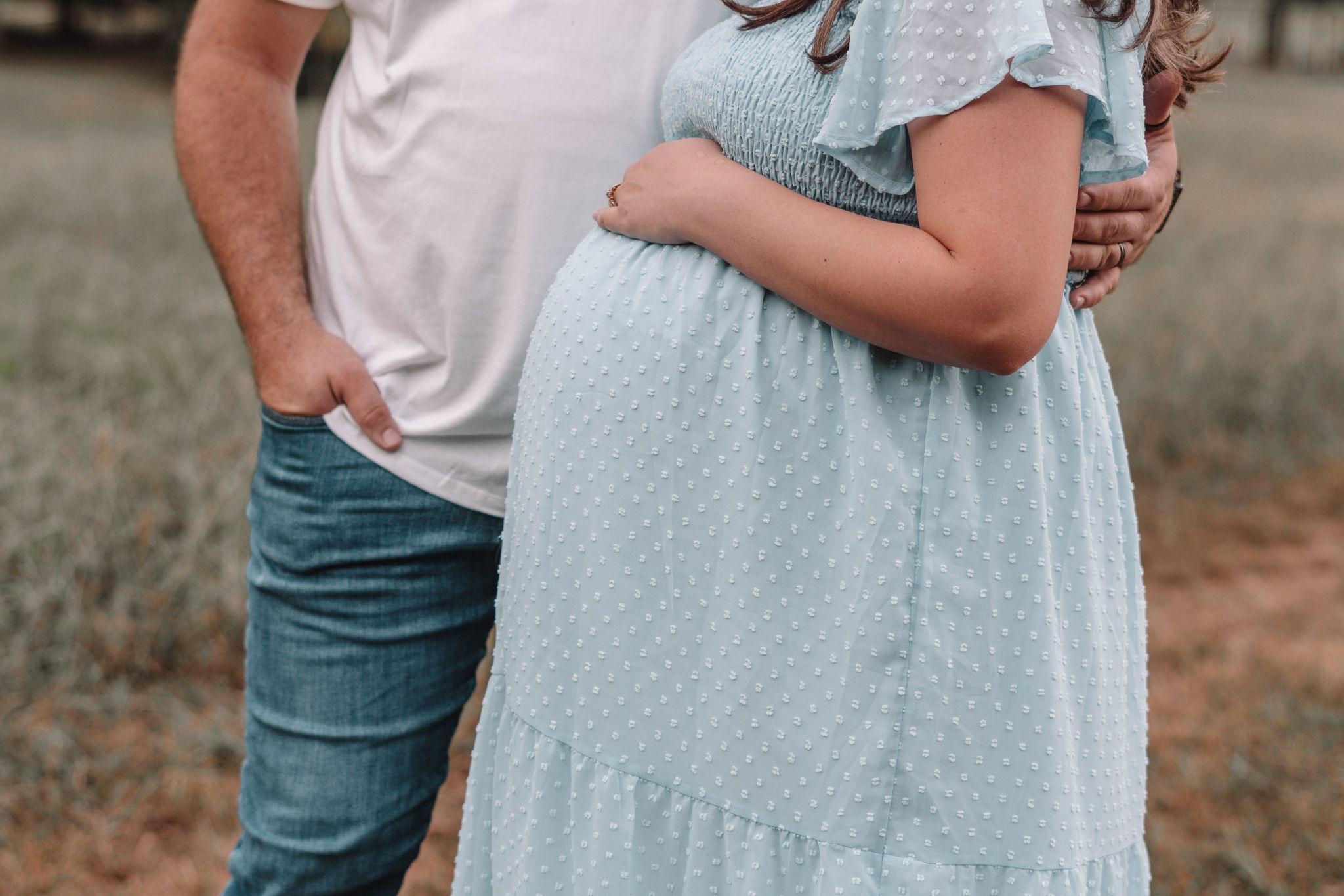Couple wearing light blue and white outfits embrace in an outdoor setting during golden hour.