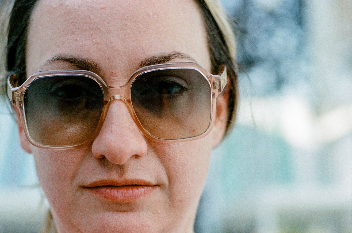 Vintage-style portrait with oversized brown gradient sunglasses against soft blurred background.