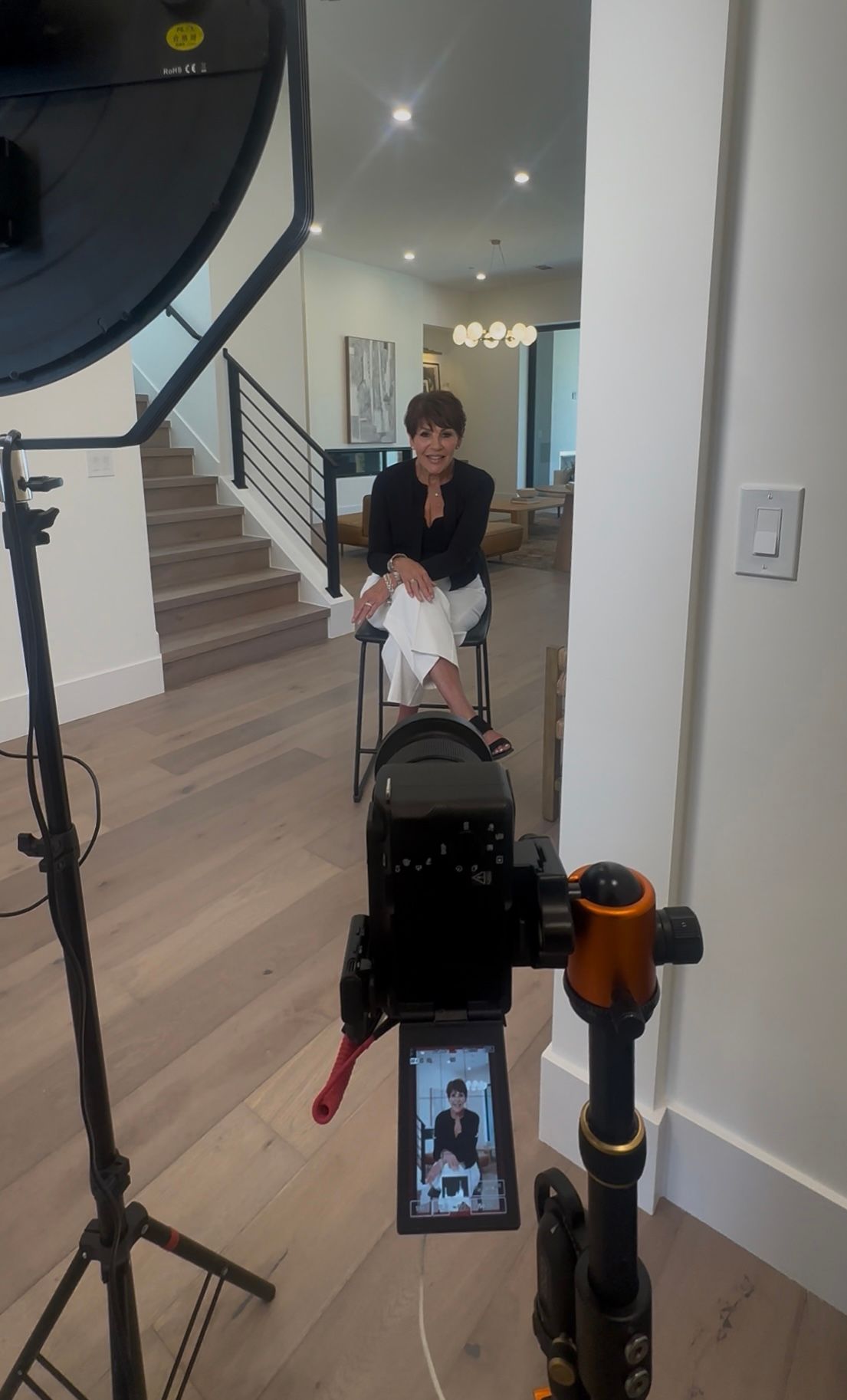 Video recording setup with camera equipment and monitor display showing someone sitting in an interior setting.