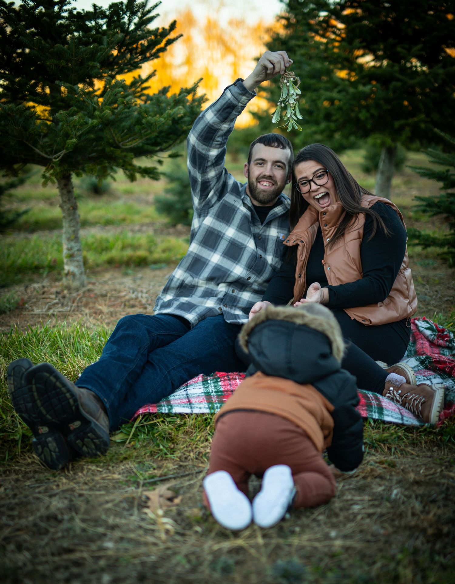 Two people enjoying a picnic on a blanket at sunset with evergreen trees in the background.