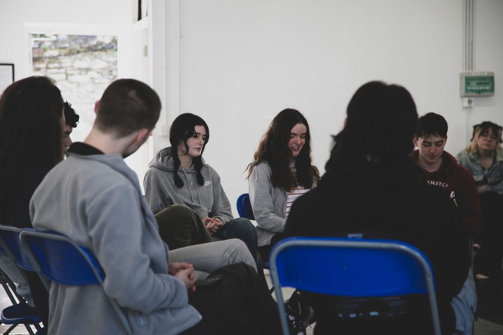 Students sit in a circle of blue chairs during what appears to be a casual classroom discussion.