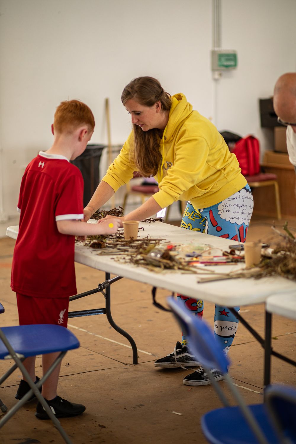 Adult in yellow jacket helps young student with hands-on activity at table during educational workshop.