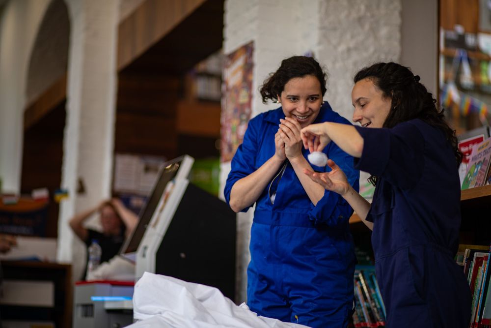 Two healthcare workers in blue scrubs react excitedly while looking at something together in a medical setting.