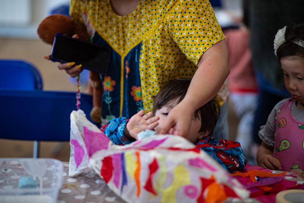 Person wearing yellow polka dot shirt crafts with colorful materials at a table with blue chairs.