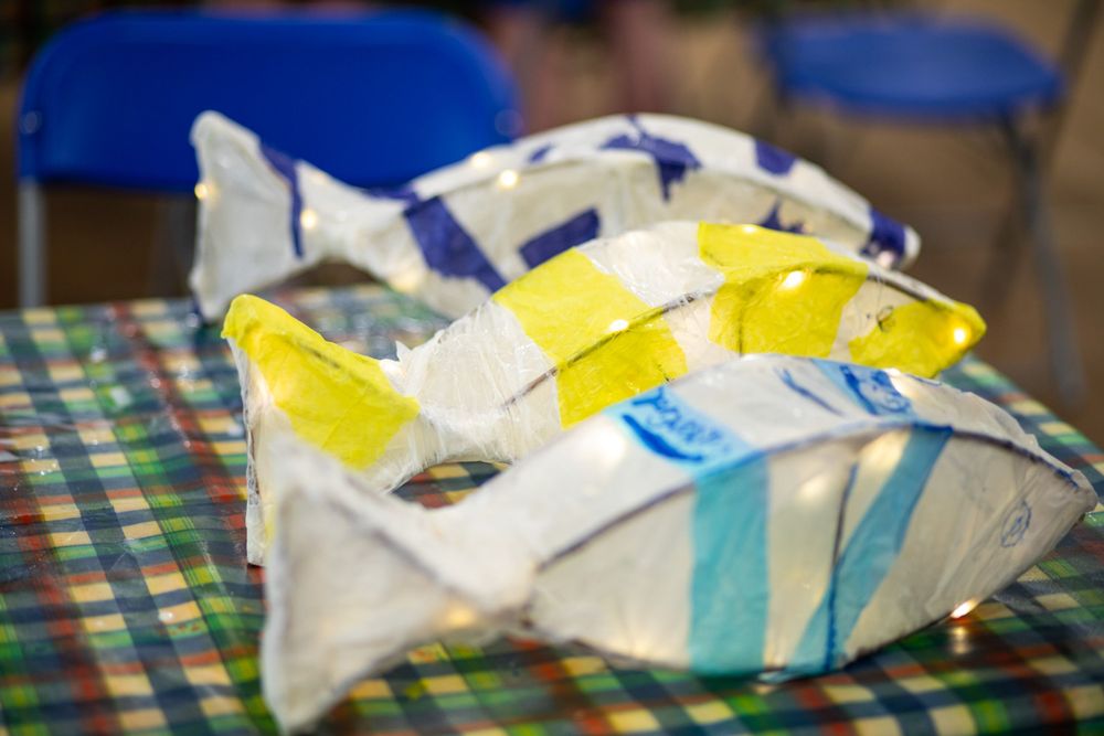 Handmade paper or fabric art project with yellow and blue stripes displayed on patterned tablecloth.