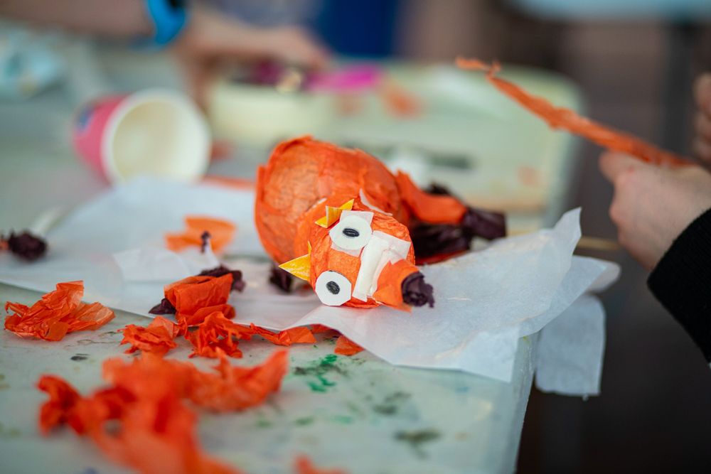 Orange plush toy being crafted or repaired on white paper with scattered orange fabric pieces nearby.