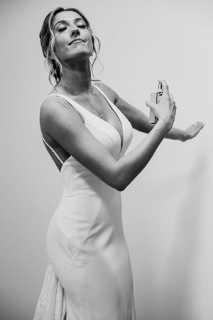 A black and white portrait of someone applying perfume while wearing an elegant white evening dress.