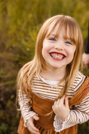 Joyful child in brown corduroy overalls and striped shirt laughs outdoors against autumn background.