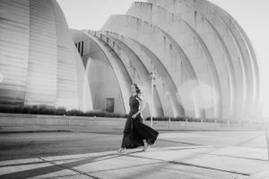 A graceful figure in a flowing black dress poses elegantly against the curved architecture of the Kauffman Center in Kansas City.