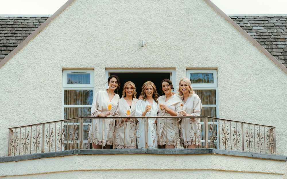 A group of people wearing matching beige robes pose together on an ornate white balcony of a light-colored building.
