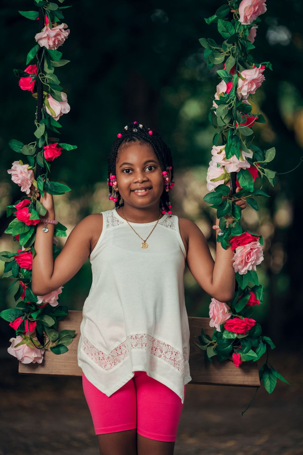Garden portrait on swing decorated with pink and red climbing roses against dark background.