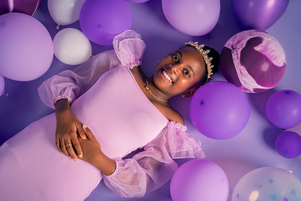 Dreamy portrait surrounded by purple and pink balloons in princess-style dress.