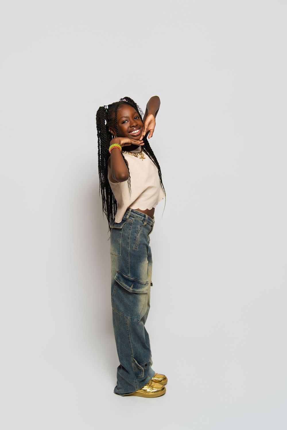 Child in overalls and yellow shoes poses playfully against a white background in a series of candid shots.