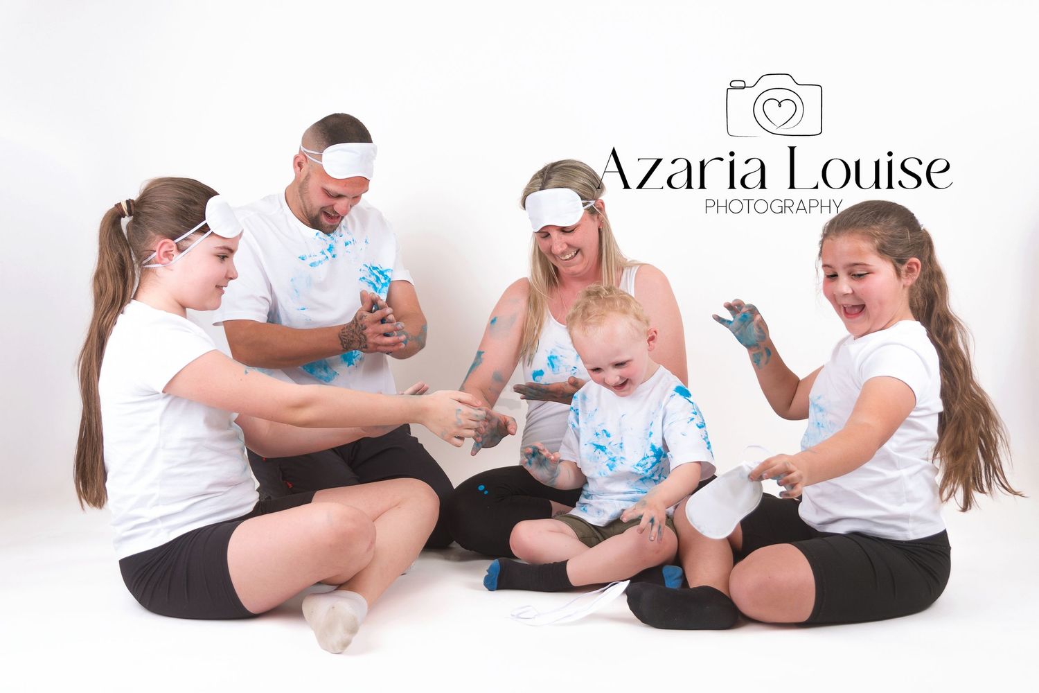 Playful group wearing matching white shirts and black shorts sit together on white backdrop in photography studio session.