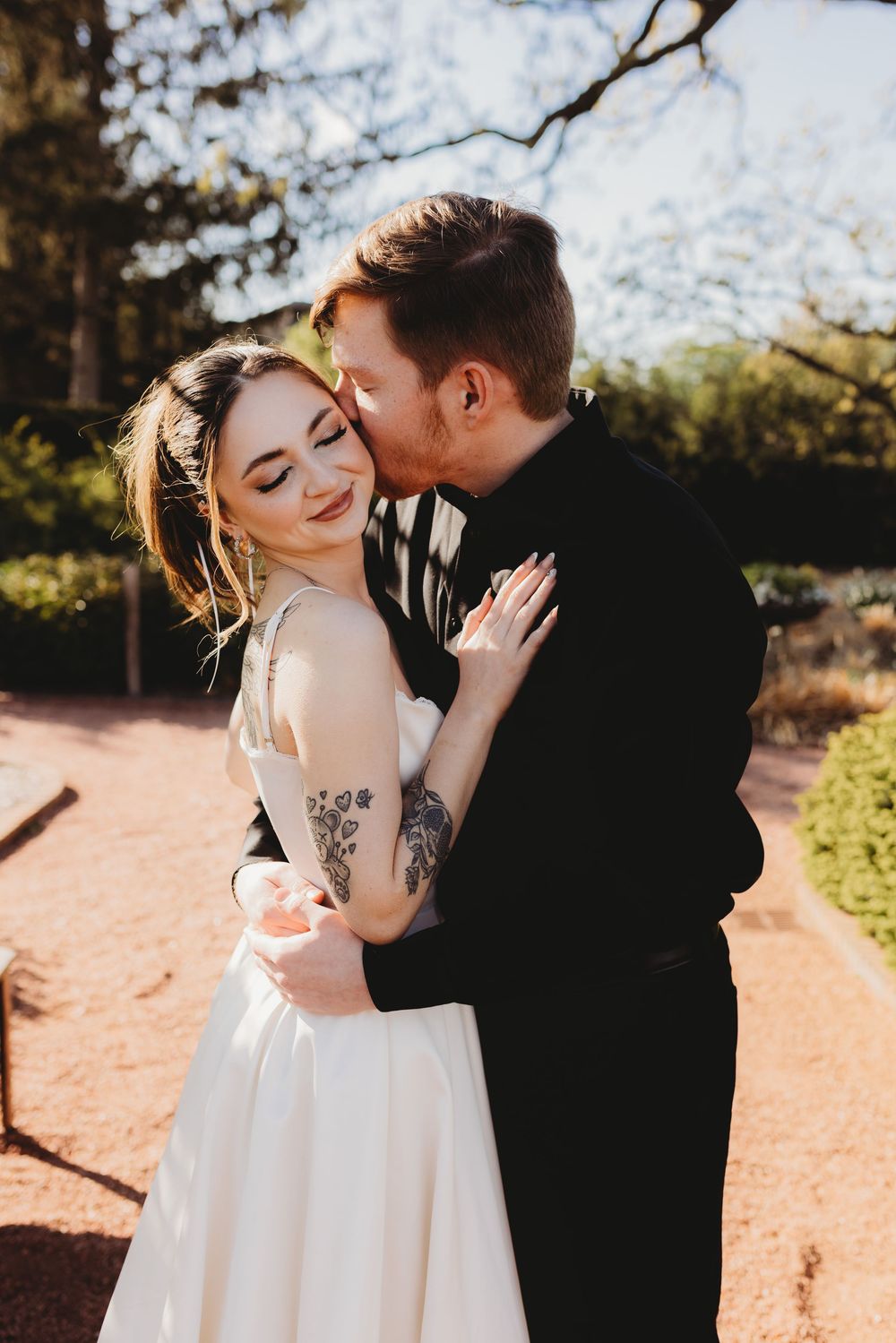 Sunlit wedding photo of couple sharing romantic moment in garden setting.