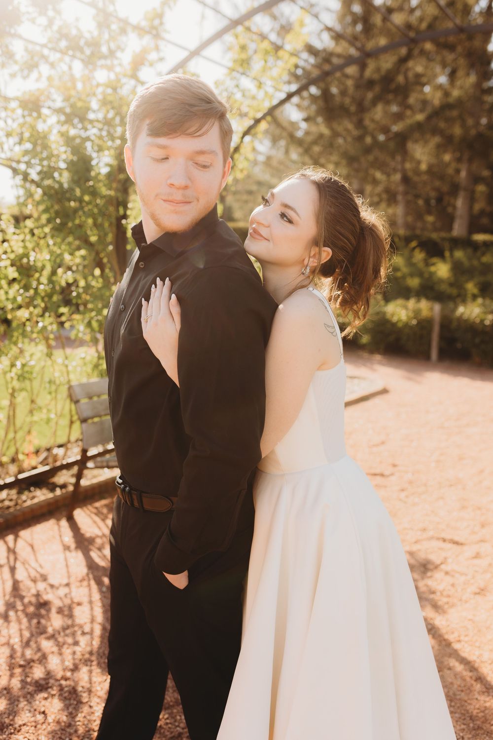 A romantic wedding couple embraces in warm sunlight during an outdoor photoshoot.