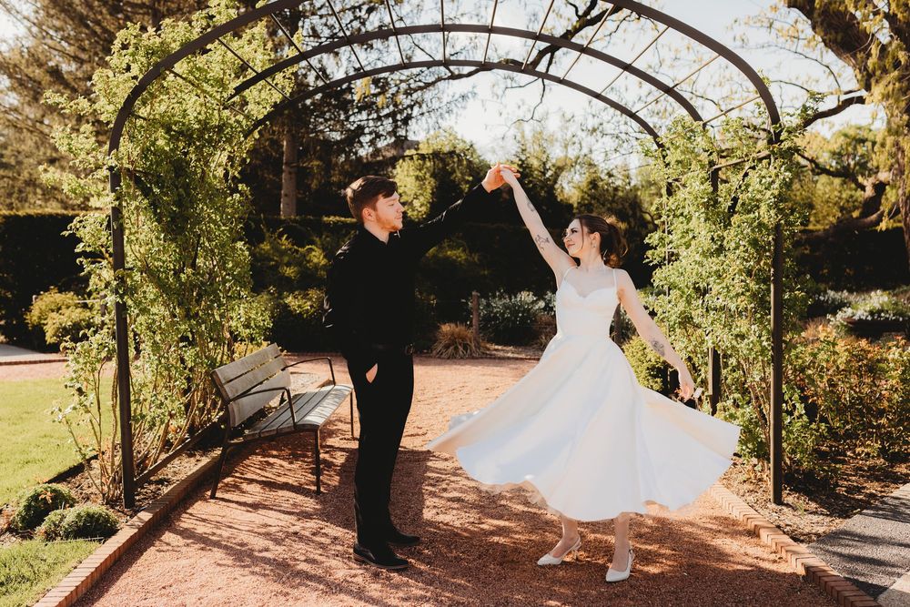 Joyful couple dancing under garden arch during wedding photoshoot.