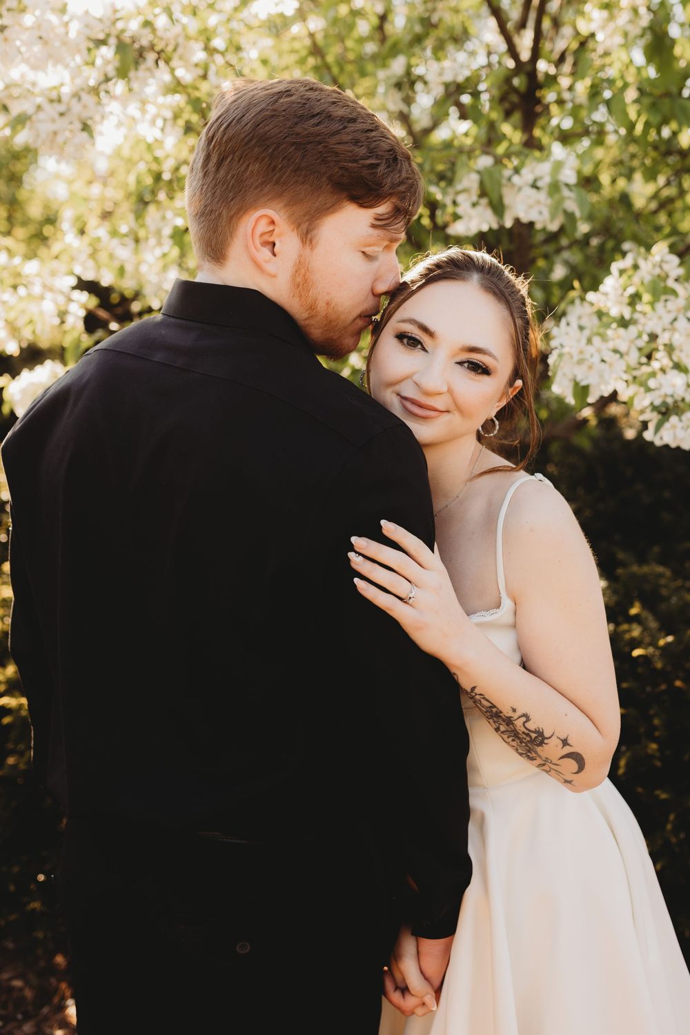 A romantic wedding couple embraces in front of blooming spring trees during golden hour.