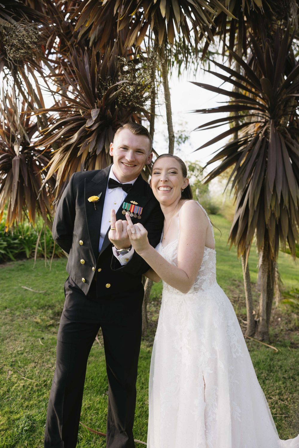 A wedding couple shares a joyful laugh together outdoors under palm trees during their celebration.