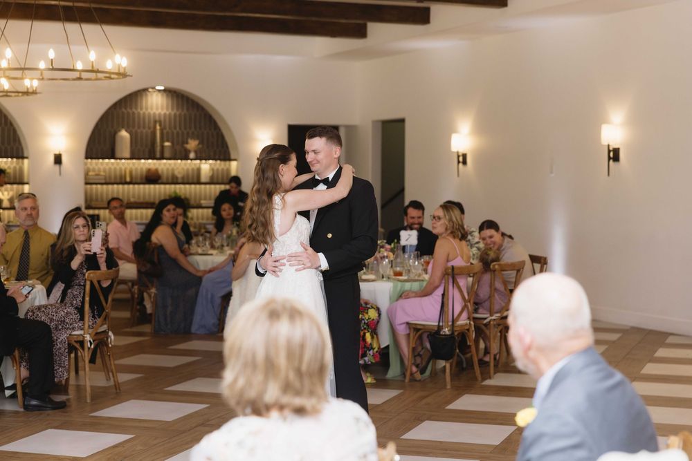 A couple shares their first dance at a wedding reception while guests watch from decorated tables in an elegant venue.