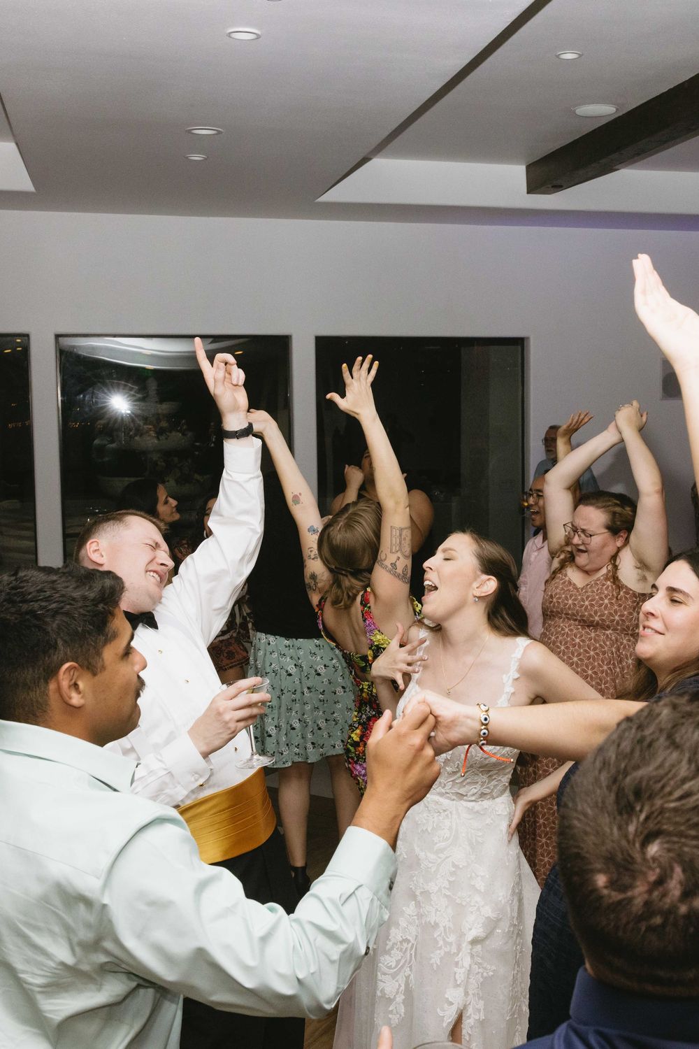 Wedding reception guests dancing and celebrating with raised arms on the dance floor during a joyous party moment.