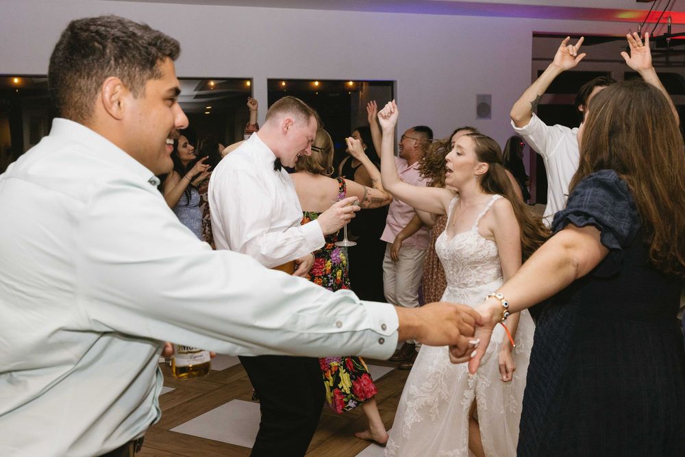 Wedding guests and newlyweds dancing energetically together on dance floor during reception celebration.