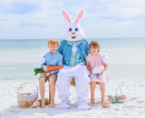 Children posing with Easter Bunny mascot on sunny beach with Easter baskets in the sand.