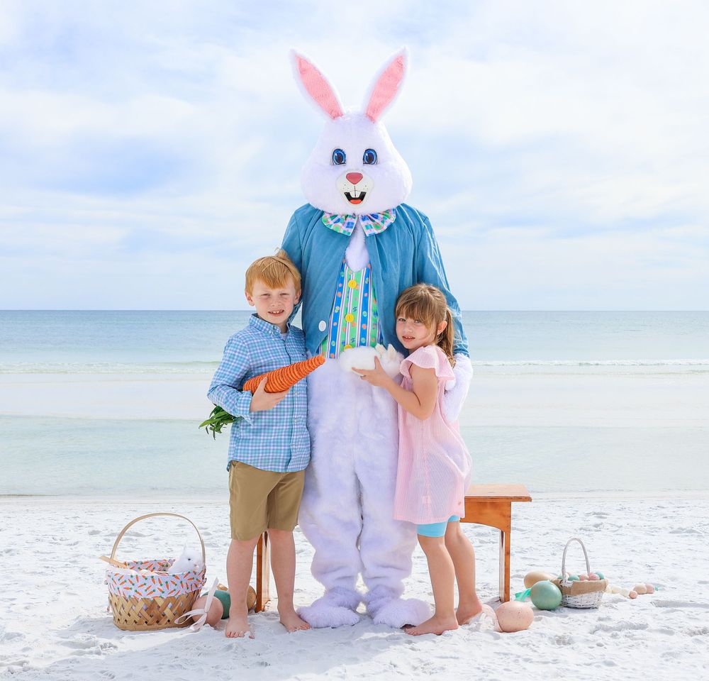 Children posing with Easter Bunny mascot on sunny beach with baskets and decorations.