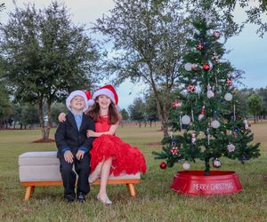 A festive outdoor Christmas photo setup with a decorated tree and red Coca-Cola crate base in a park setting.