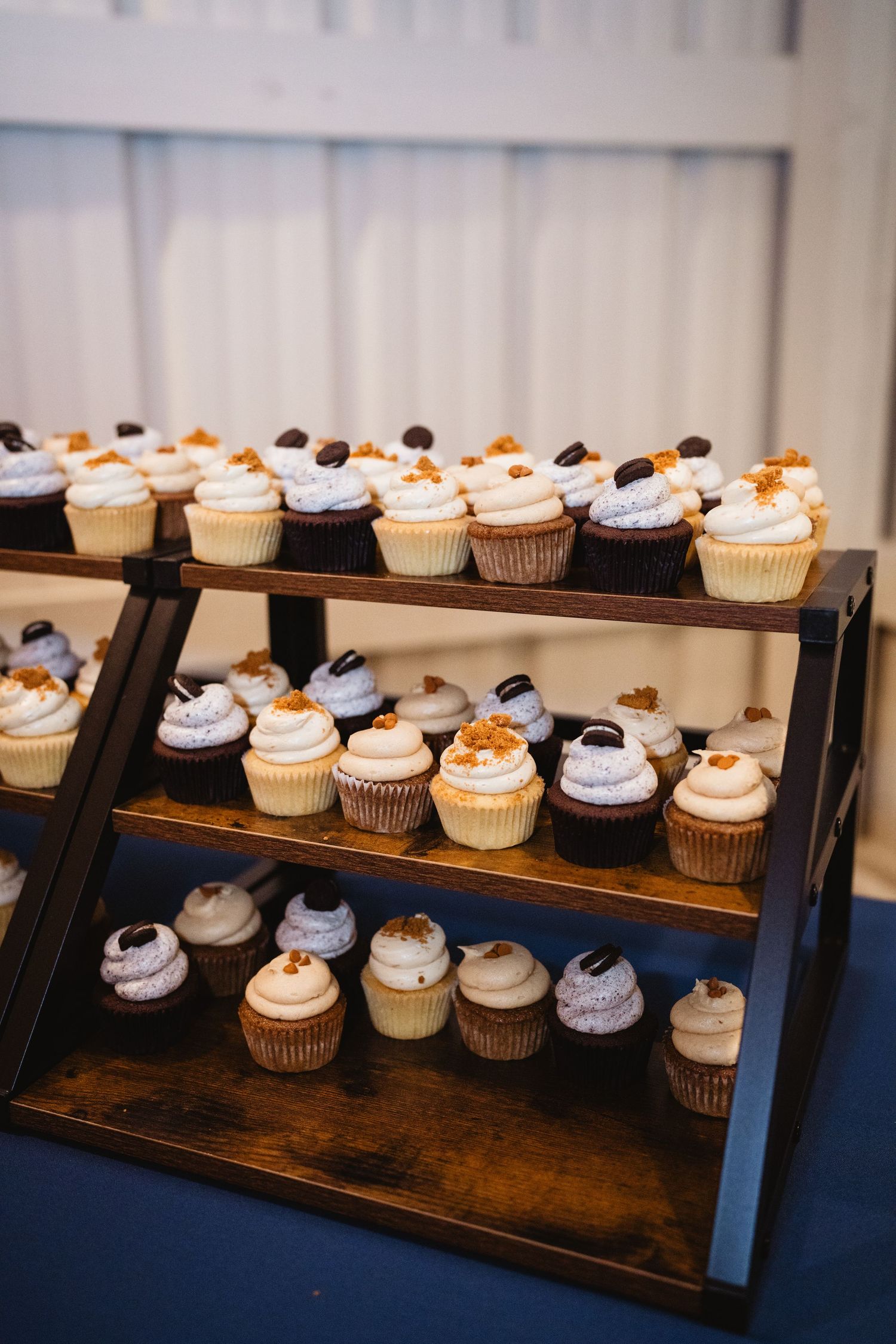 An assortment of decorated cupcakes displayed on a rustic three-tiered wooden stand with chocolate and vanilla frosting.