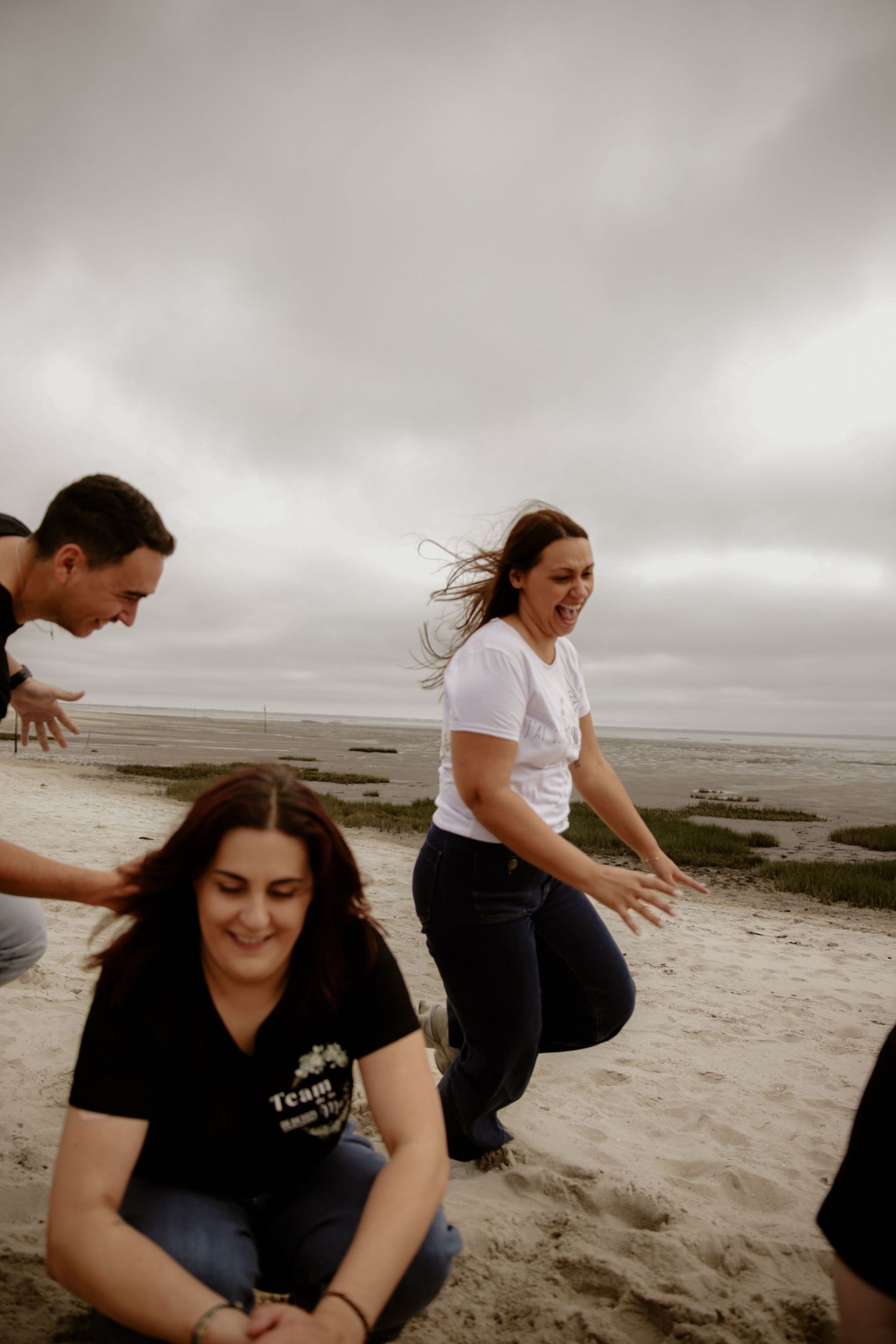 Friends enjoy a fun and candid moment playing together on a cloudy day at the beach.