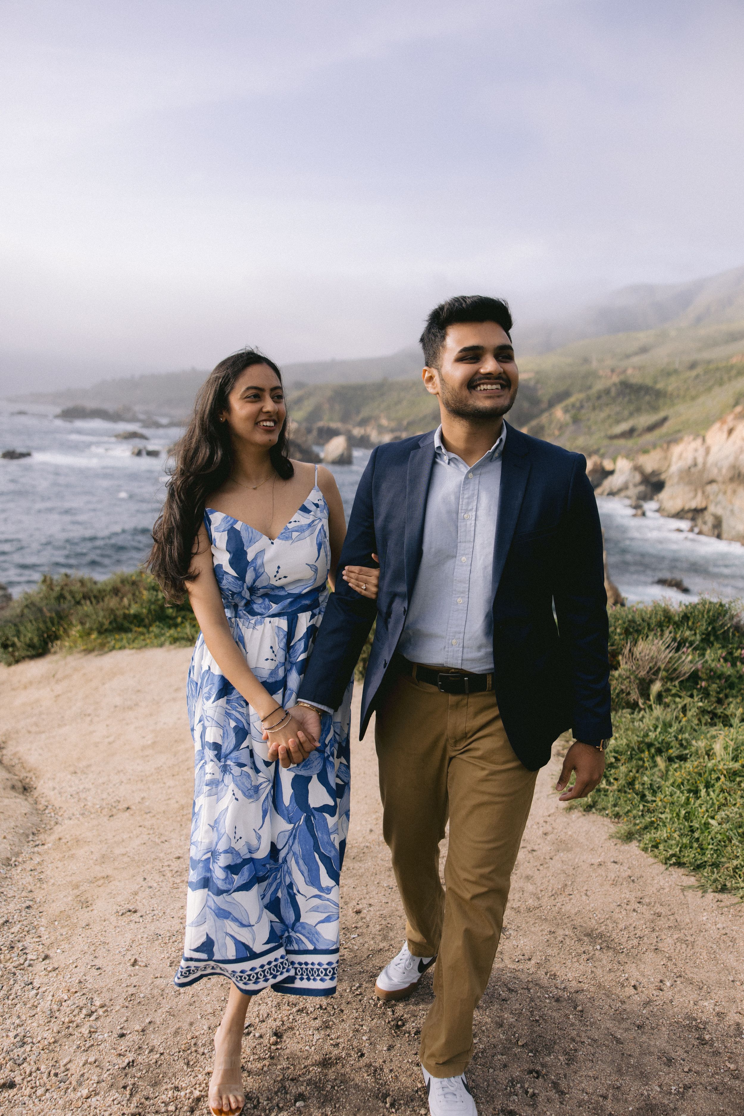Couple dancing together on a coastal hiking trail overlooking Big Sur's dramatic cliffs and ocean views.