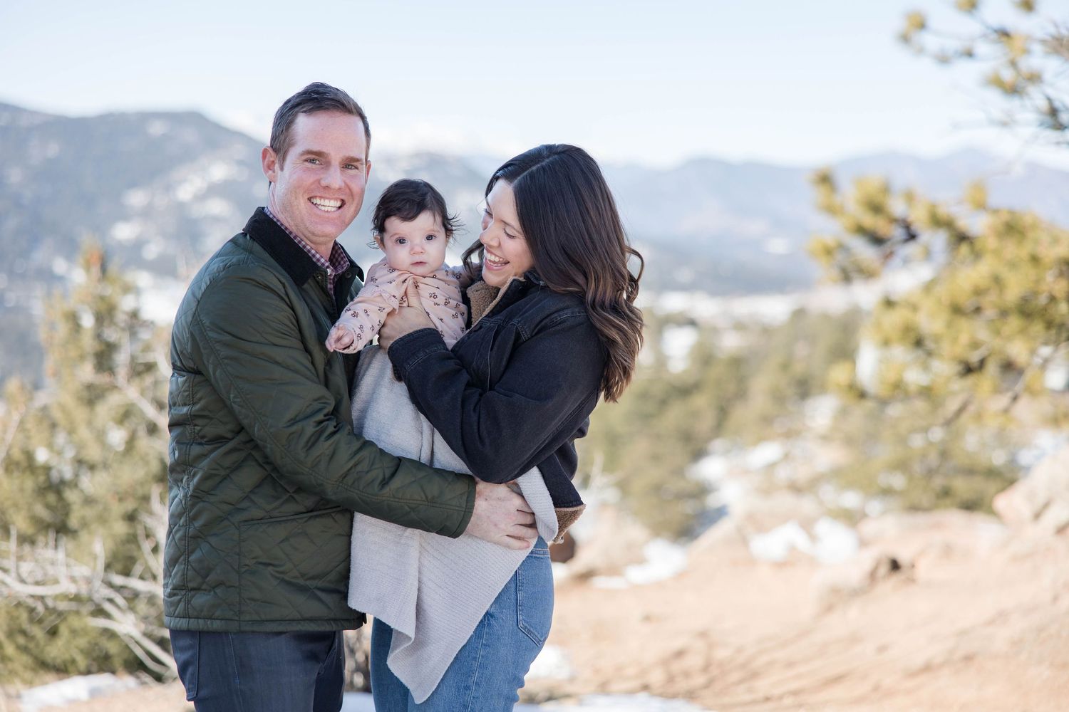 A family shares a joyful moment together while posing outdoors in the snowy winter mountains.