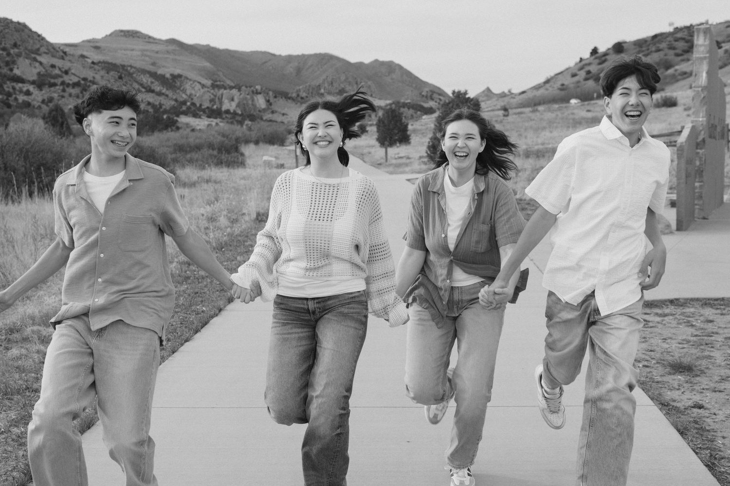 Group of young Asian friends holding hands and running together outdoors in black and white photo.
