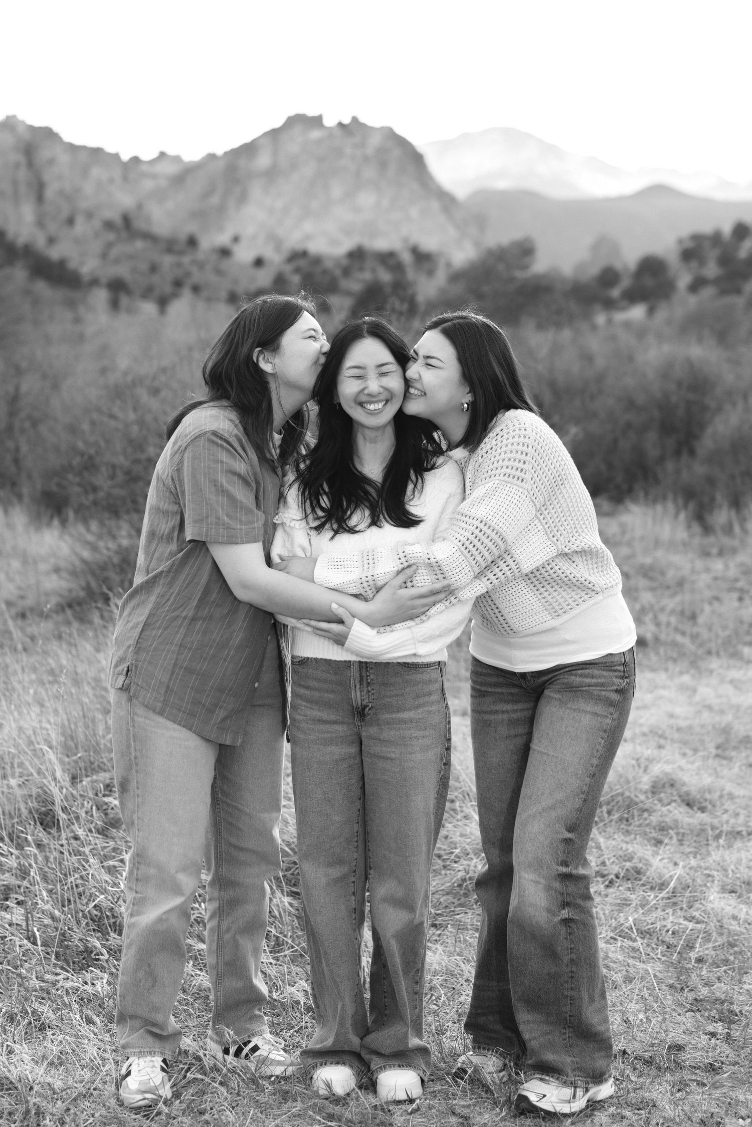 Three young women laughing together outdoors with mountain scenery in black and white photo.