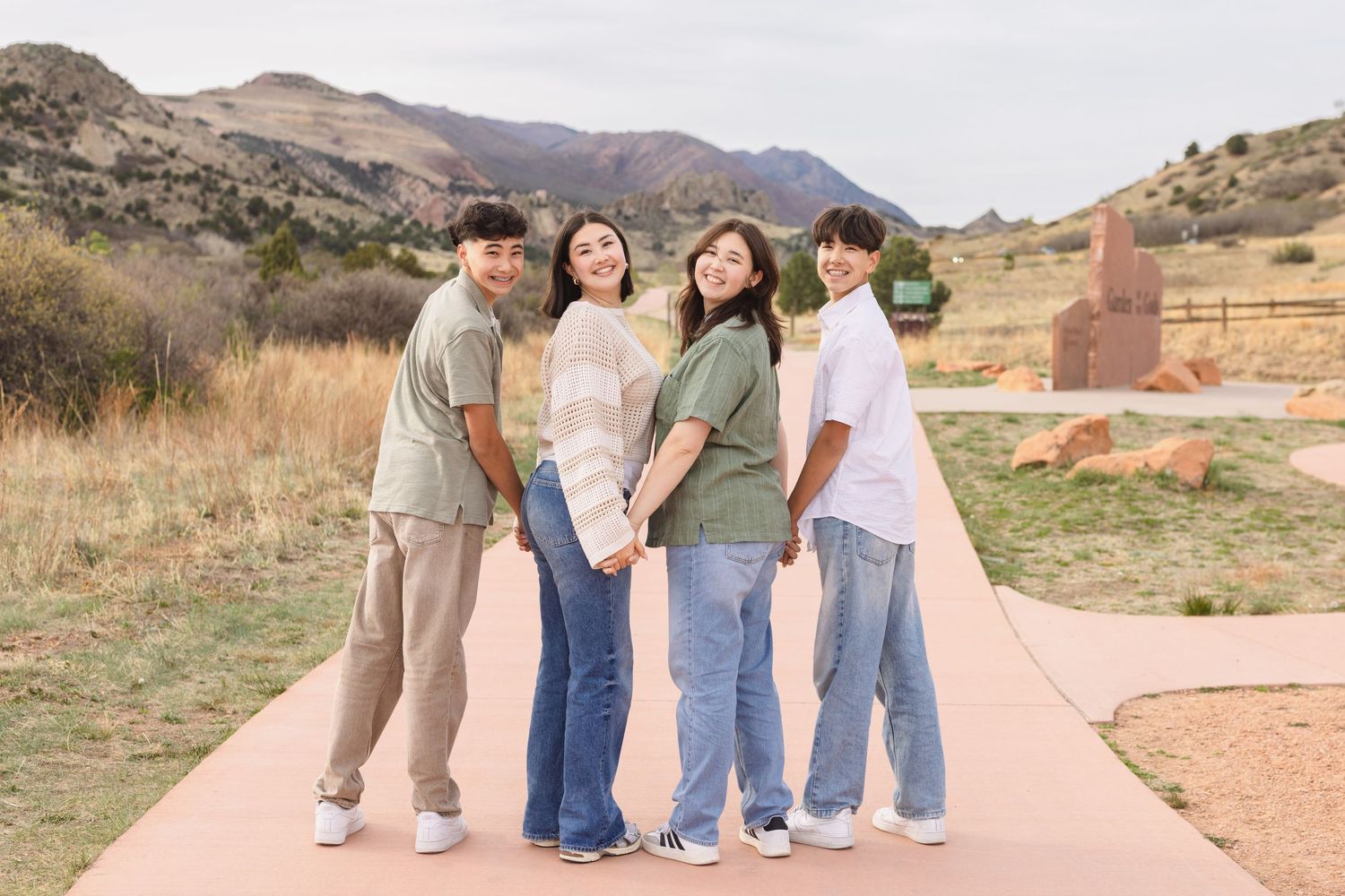Four young adults pose together on a scenic path with mountains and golden fields in the background.