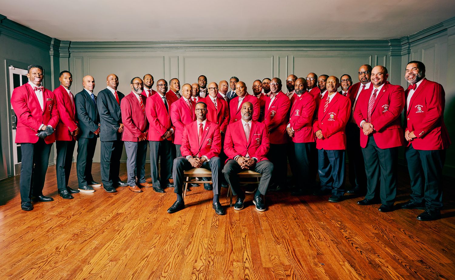 Large group of men in matching red blazers and dark pants posing for formal group portrait.