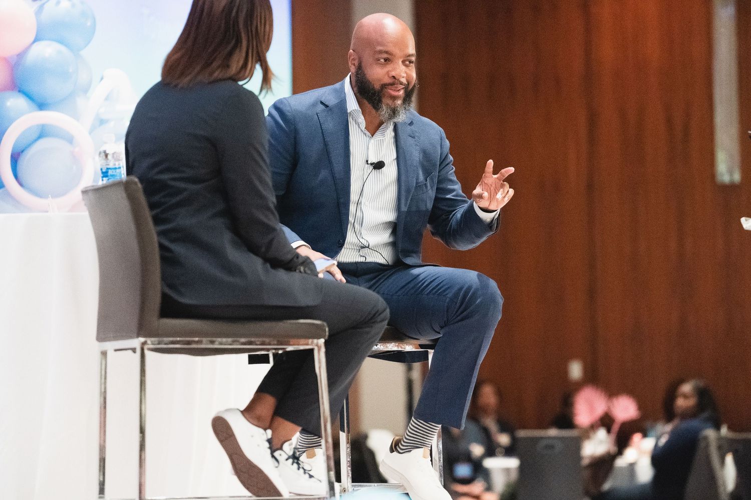 Two speakers engage in a panel discussion on stage at a professional conference in a large auditorium.