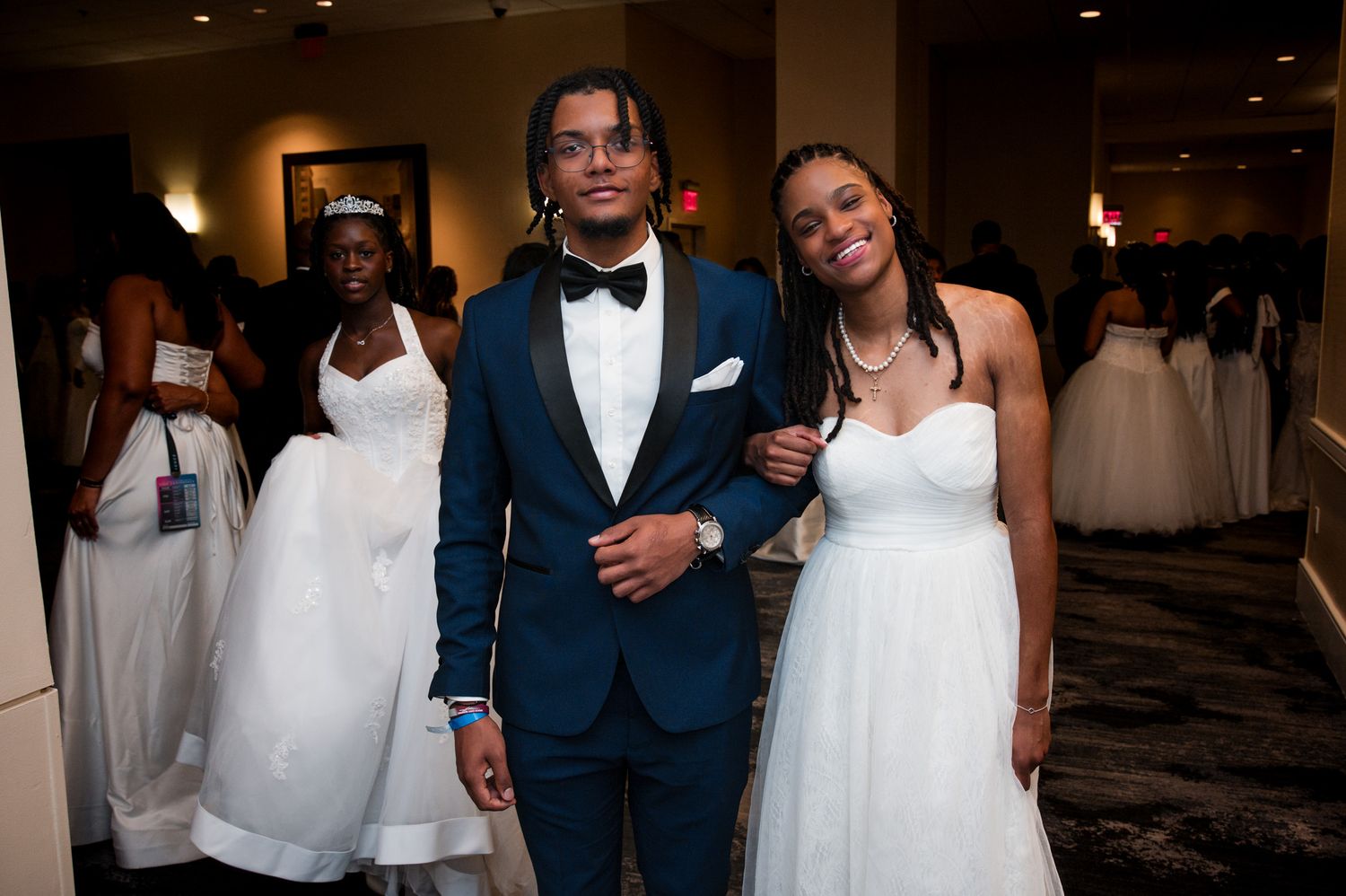 Young Black couple posing together at a formal debutante ball, man in teal suit, woman in white gown.