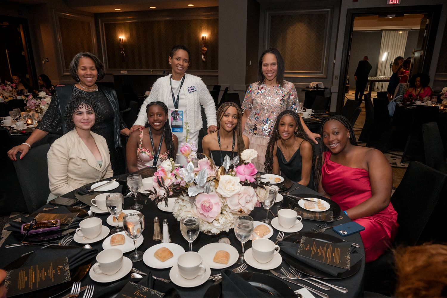 Group of women posing together at an elegant banquet table with floral centerpiece at a formal gala event.