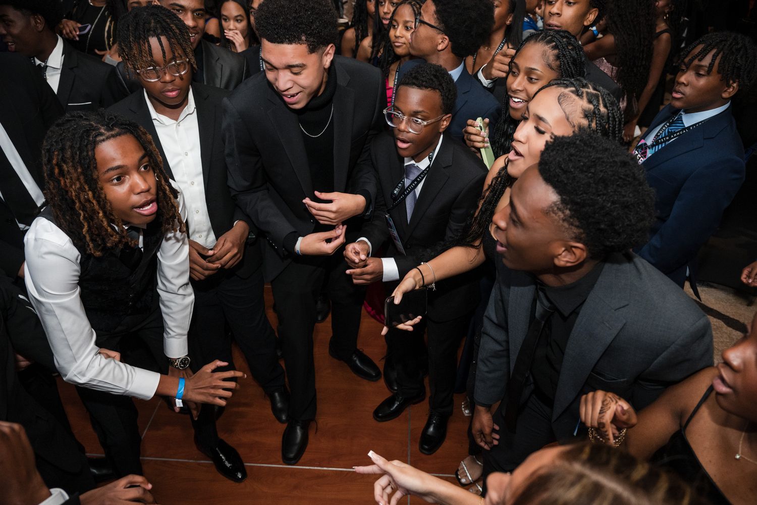 Young men in formal attire socializing and dancing together at an elegant evening event.