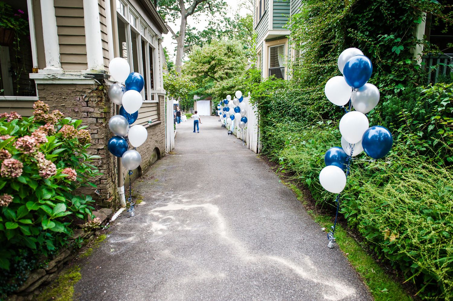 Blue and white balloon arrangements line a pathway leading to a house entrance.