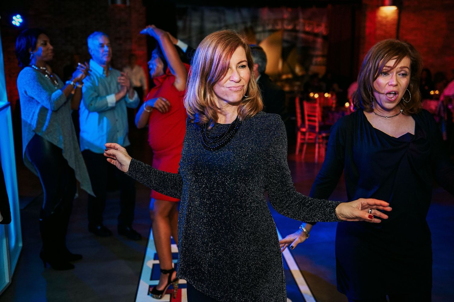 Women dancing at a vibrant indoor party with guests cheering in the background, capturing lively moments in professional event photography.