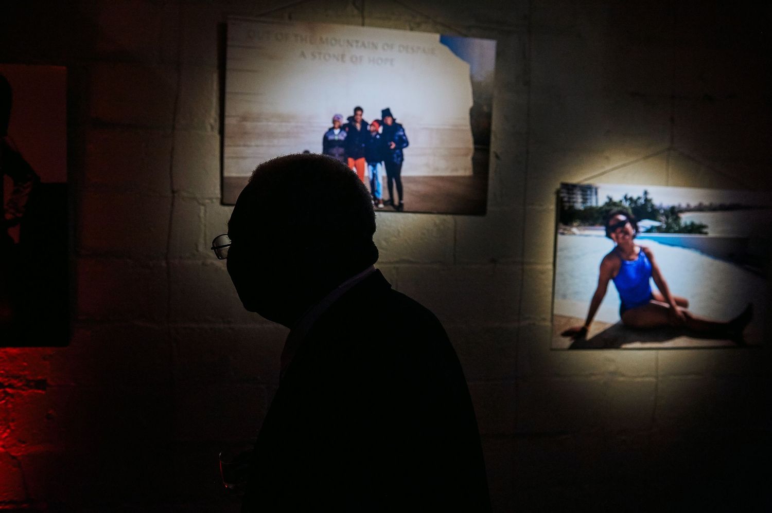 Silhouette of person viewing illuminated photo exhibition display on a stone wall.