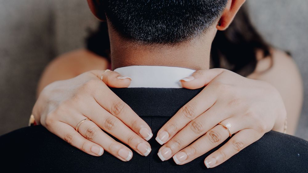 A close up view of hands with white nail polish gently resting on the back of someone's neck.