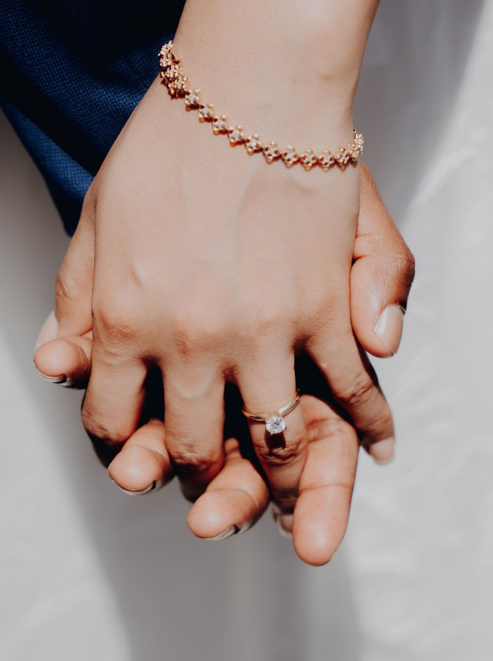 Close-up of two hands holding each other, with one wearing a delicate rose gold bracelet and an engagement ring.